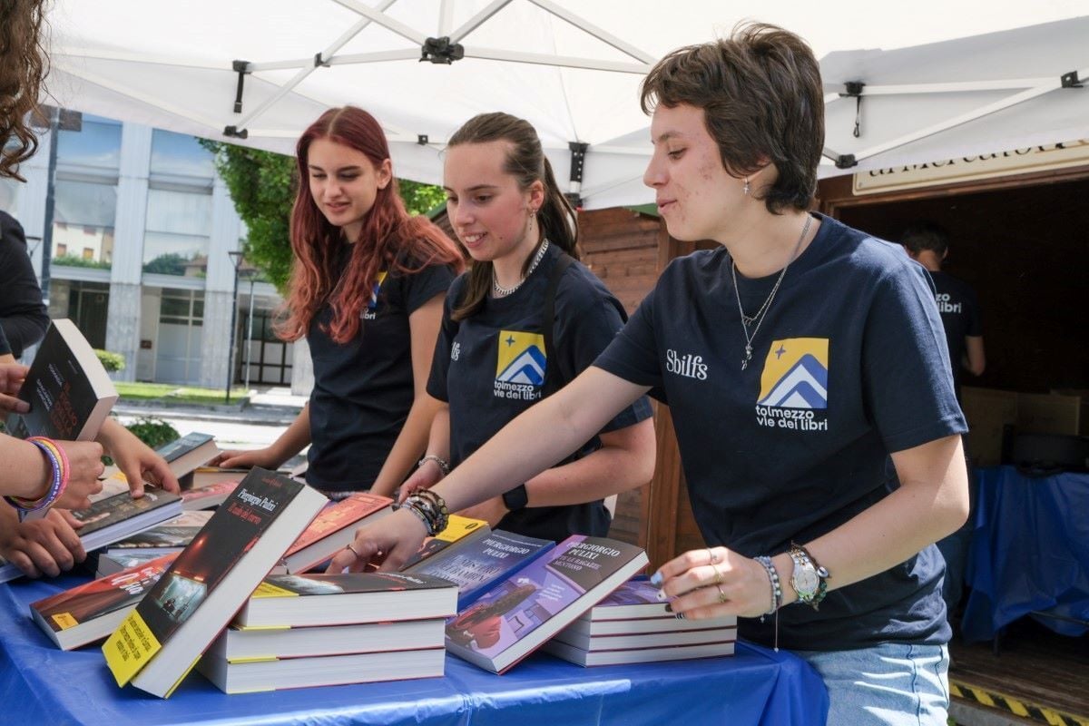 Un gruppo di giovani membri dello staff di Tolmezzo vie dei libri davanti a una bancarella di libri